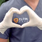 Eine Person in Pflegekleidung formt mit behandschuhten Händen ein Herz. Auf der Kleidung ist das Logo ‚ELFIN care‘ zu sehen. Die Geste steht symbolisch für Fürsorge und Zusammenhalt.
