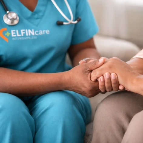 Hand halten (472 x 472 px) Pflegekraft in türkisfarbener „Elfin Care Intensivpflege“-Kleidung hält beruhigend die Hand einer Patientin Symbolbild für ambulante Intensivpflege zu Hause und persönliche Betreuung im vertrauten Umfeld.